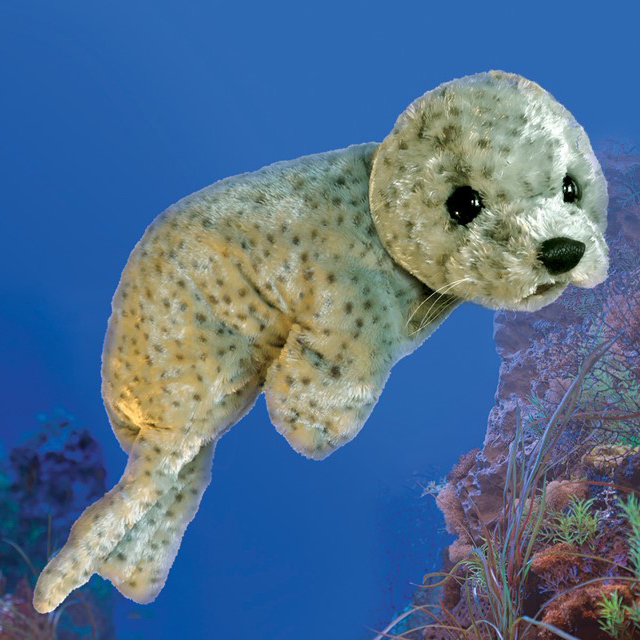 Folkmanis Handpuppe Seehund in hellgrauem Fell mit dunklen Flecken, schwarzen Glasaugen und Schnurrhaaren, vor blauem Meereshintergrund