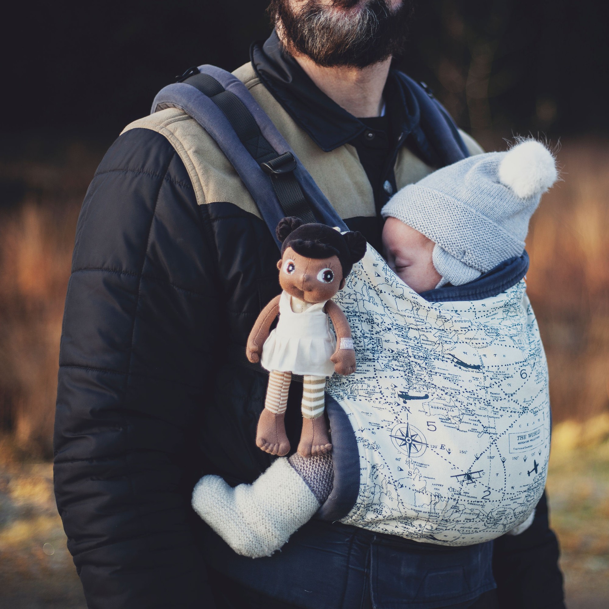 Die Rubens EcoBuds Mini-Puppe Flora steckt in einer Babytrage neben einem Baby
