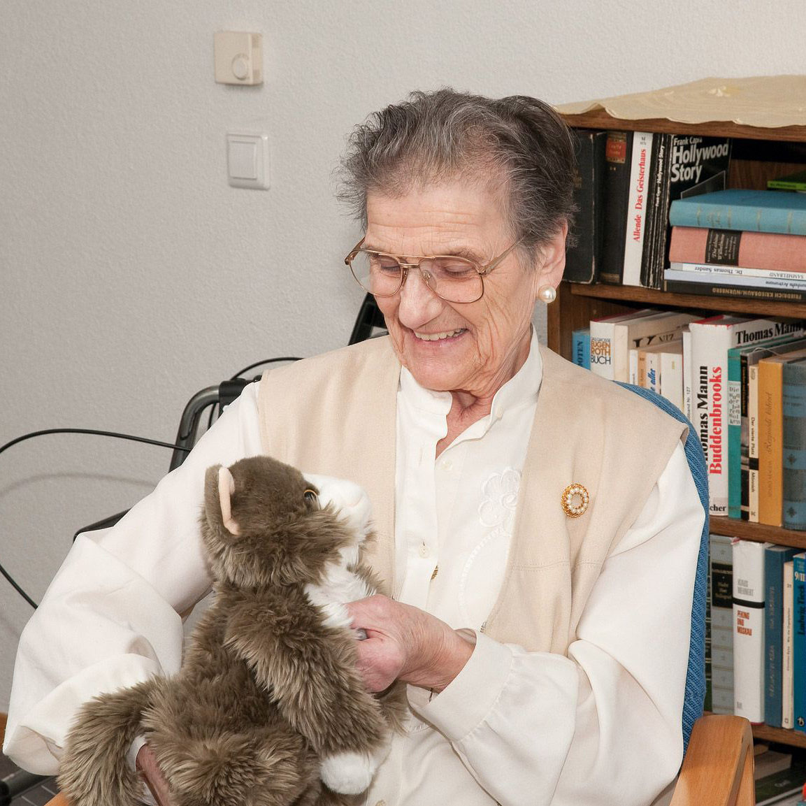 Seniorin streichelt die Joyk Empathiepuppe Billy in einem Wohnzimmer