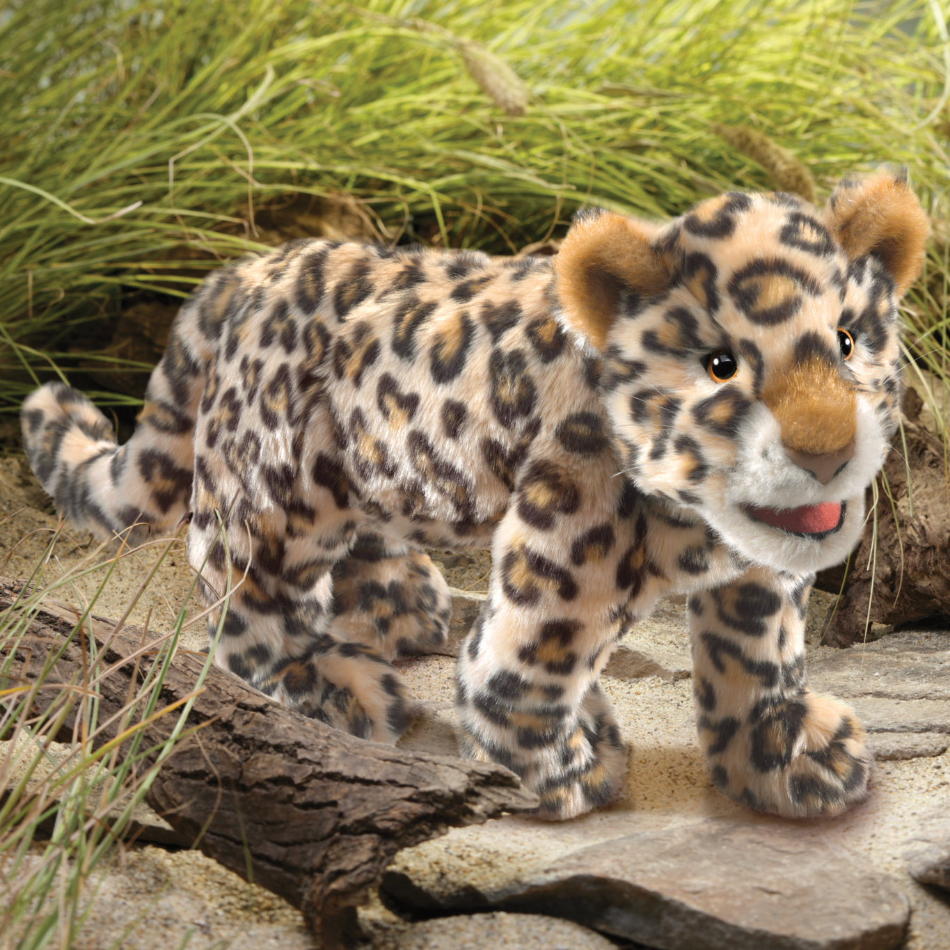 Folkmanis Handpuppe Leoparden-Baby mit beigem Fleckenfell, orangefarbenen Ohren und geöffnetem Maul, stehend auf Steinen vor Gras