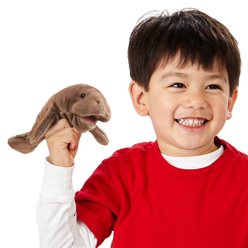 Smiling boy holding a brown Folkmanis mini manatee finger puppet up on his index finger