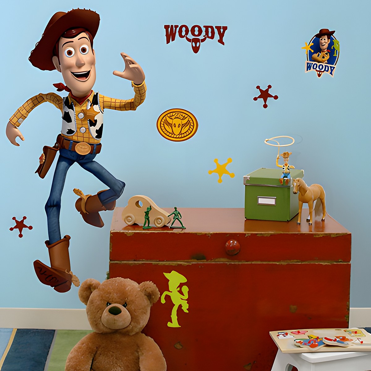 RoomMates wall decal Disney Pixar Toy Story Woody, Woody in a jumping pose with a cowboy hat on a blue children's room wall above a red chest with a teddy bear