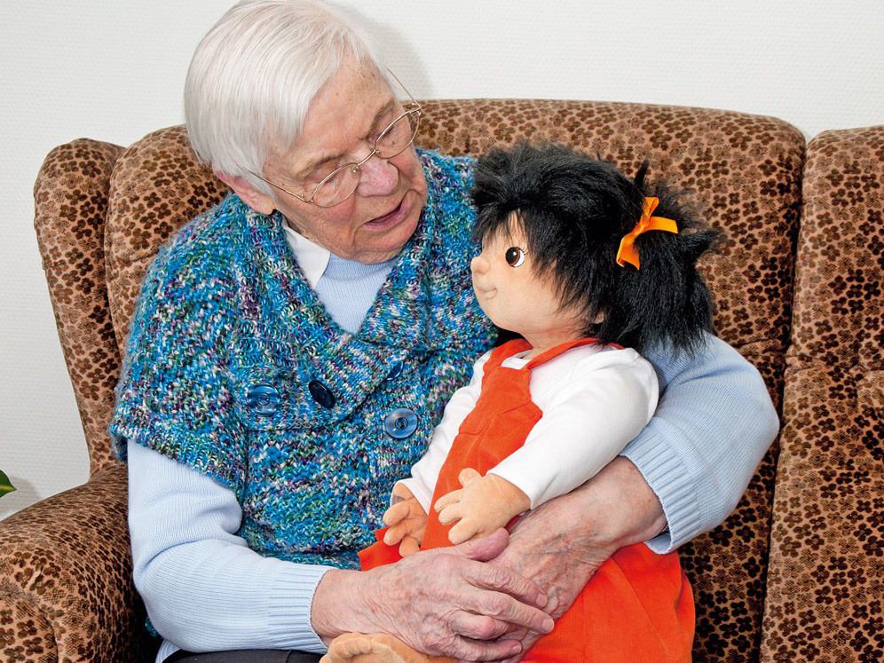 Seniorin hält die Joyk Empathiepuppe Emelie im Arm