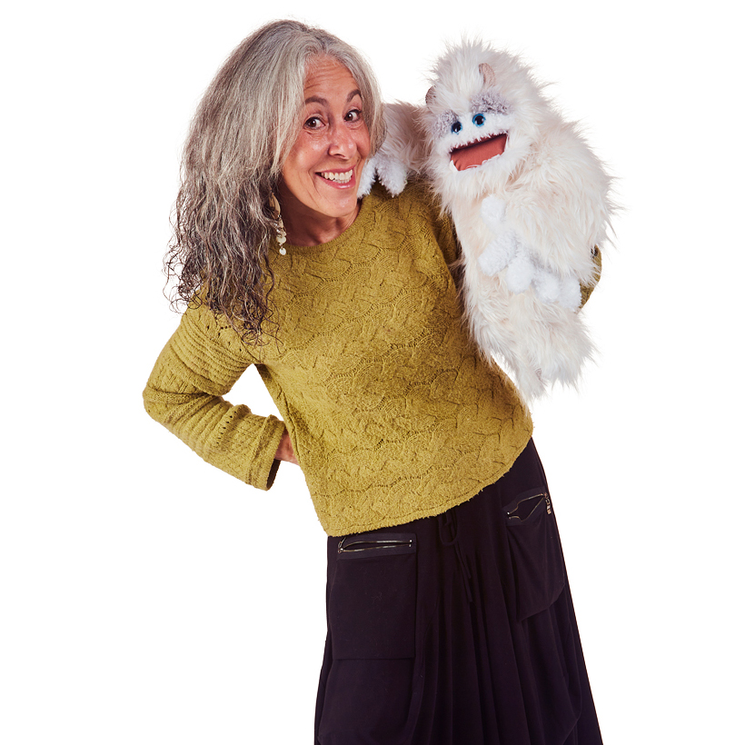Frau führt die weißfellige Folkmanis Handpuppe Yeti mit blauem Blick und beweglichem Mund an der rechten Hand.