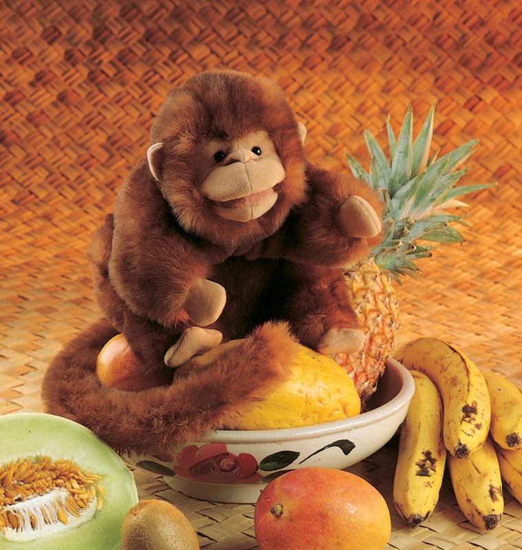 Folkmanis brown plush monkey hand puppet sitting in a fruit bowl and holding a pineapple in one hand
