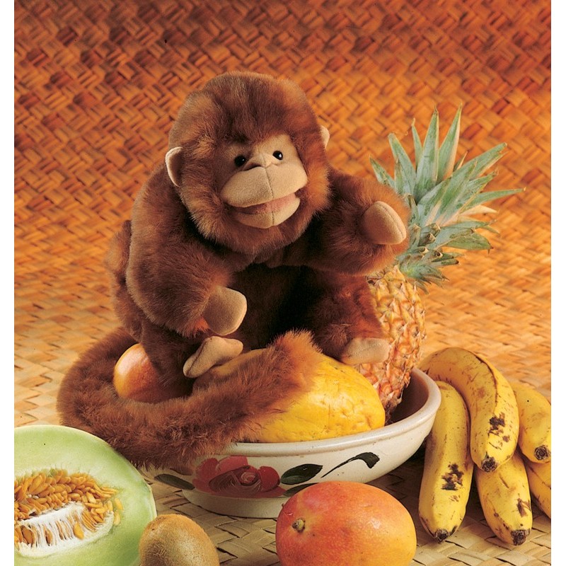 Folkmanis Handpuppe Affe aus braunem Plüsch sitzt in einer Obstschale und hält eine Ananas in der Hand.