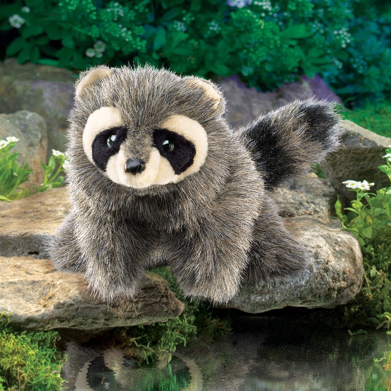Folkmanis baby raccoon hand puppet with grey-black fur and characteristic face mask, sitting on a stone