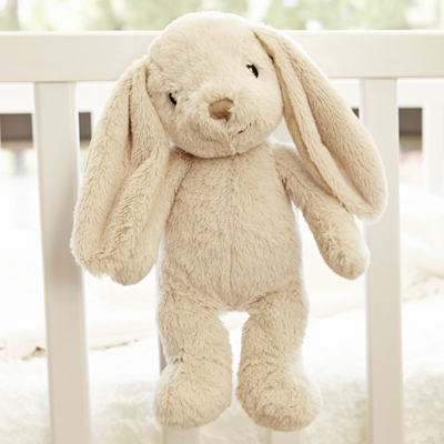 Cloud b Einschlafhilfe Bubbly Bunny, Anwendungsfoto: beiges Hasen-Kuscheltier hängt am Gitterbett