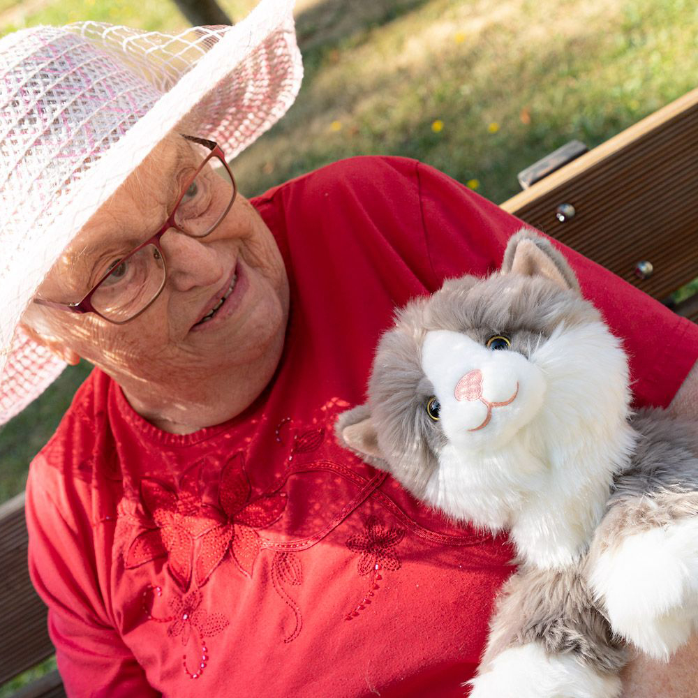 Seniorin mit der Joyk Empathiepuppe Billy im Arm auf einer Parkbank