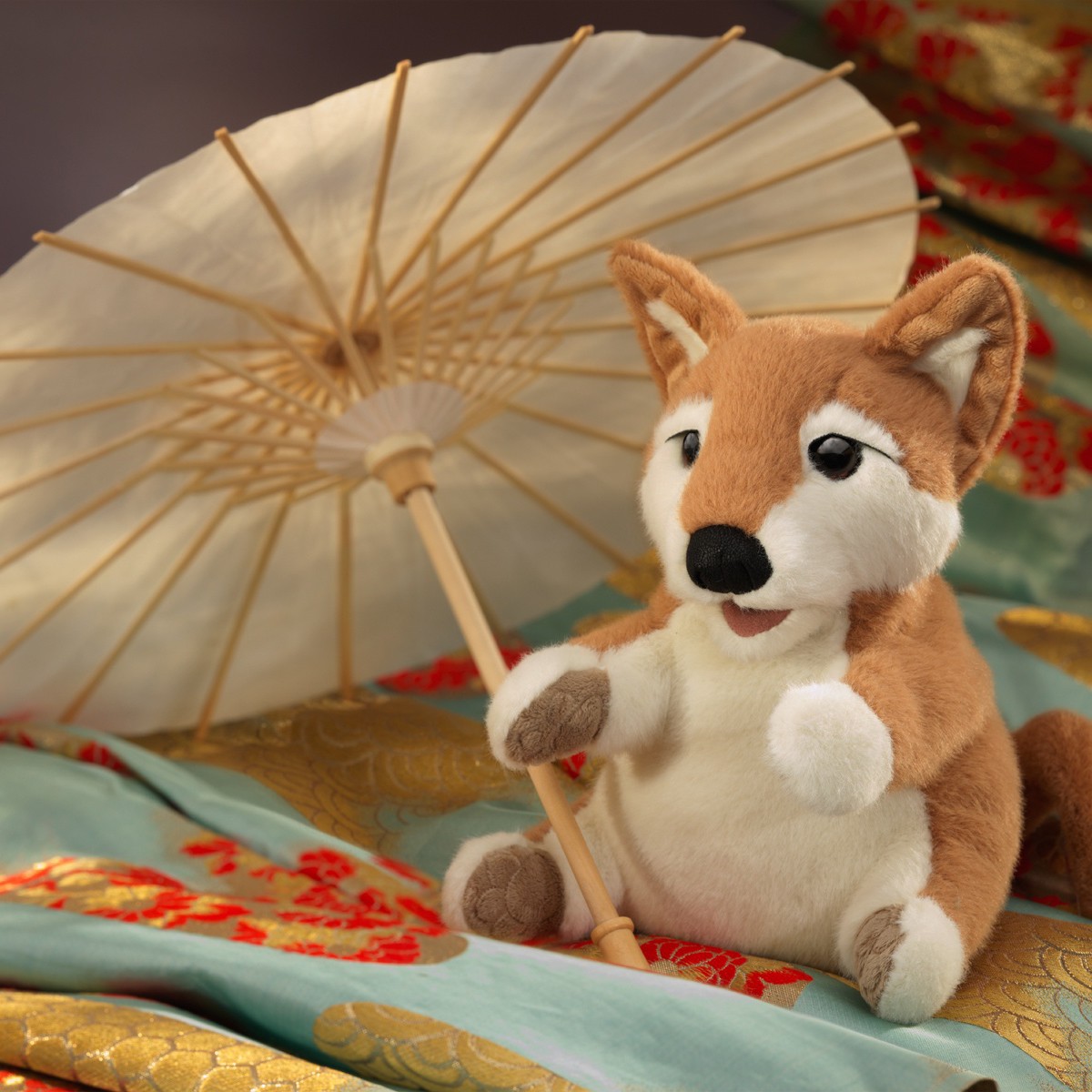 Folkmanis Handpuppe Shiba Inu in Braun-Weiß, sitzend, hält einen Papierschirm, auf bestickten Seidenstoffen in Gold und Türkis