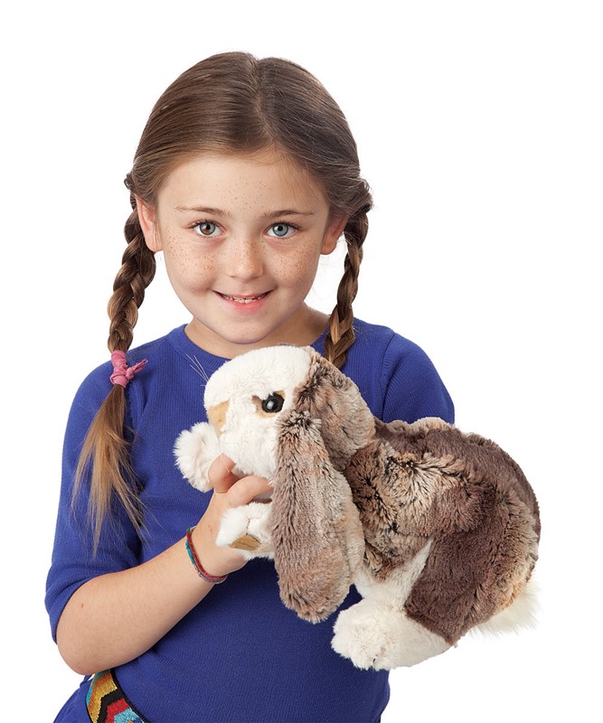 Mädchen hält Folkmanis Handpuppe Widderkaninchen-Baby mit braun-weißem Fell und langen Schlappohren in die Kamera.