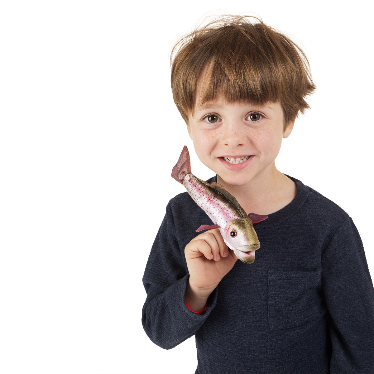 Boy holding a Folkmanis mini rainbow trout finger puppet with open mouth on his index finger, pink-green plush fish design