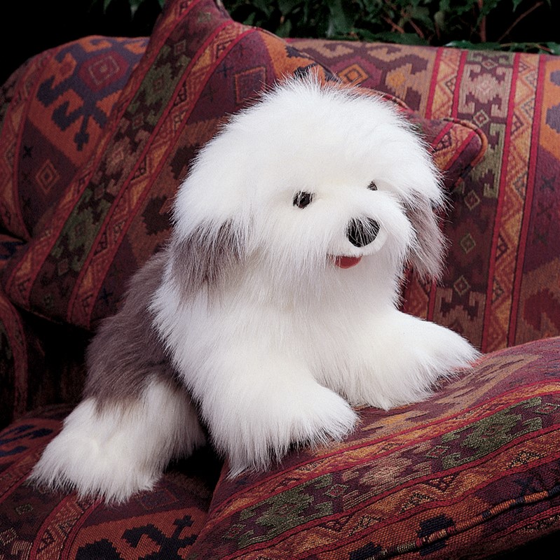 Folkmanis Handpuppe Bobtail mit weiß-grauem Zottelfell und roter Zunge sitzt frontal auf gemustertem Sofa