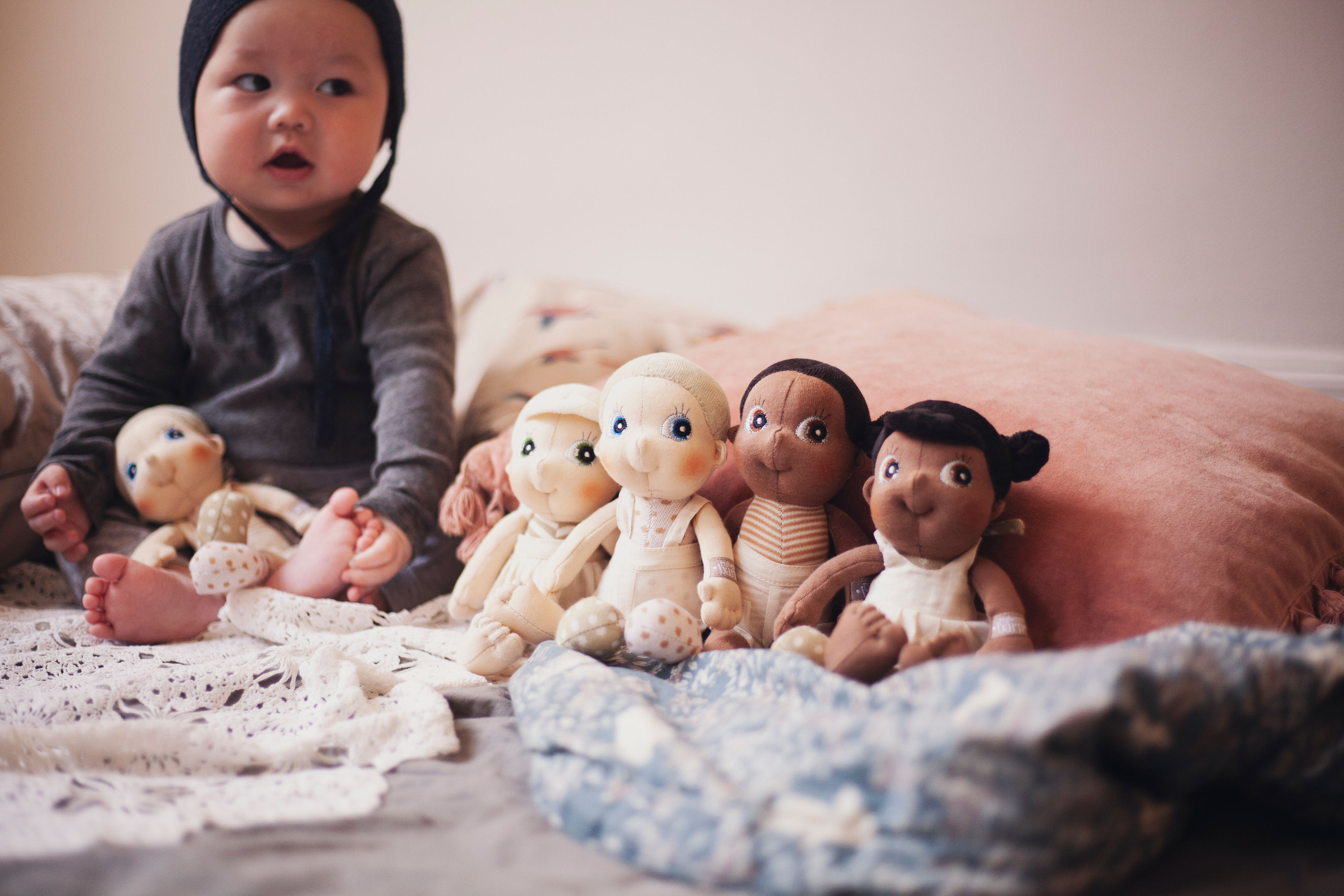 Baby sitting next to a row of Rubens EcoBuds mini dolls on the bed