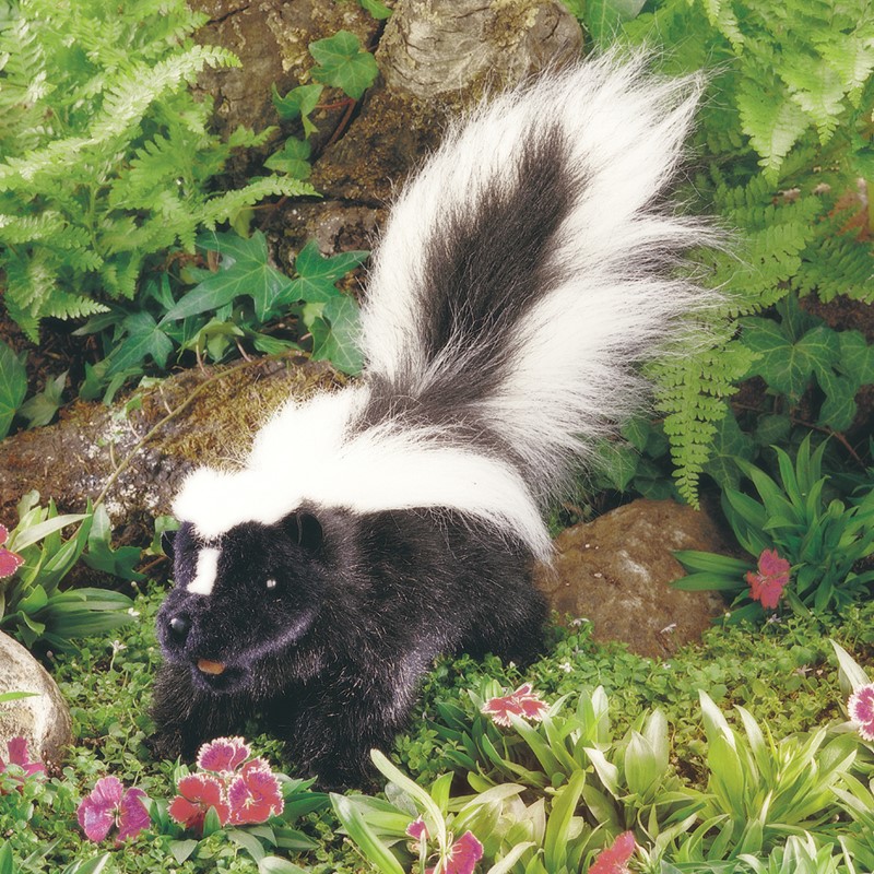 Folkmanis Handpuppe Stinktier mit schwarz-weißem Fell und buschig aufgestelltem Schwanz, Seitenansicht in Gartenkulisse