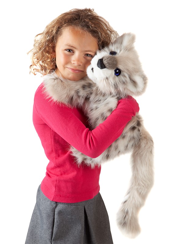 Mädchen hält Folkmanis Handpuppe Baby Schneeleopard mit grau-weißem Fell und dunklen Flecken im Arm.