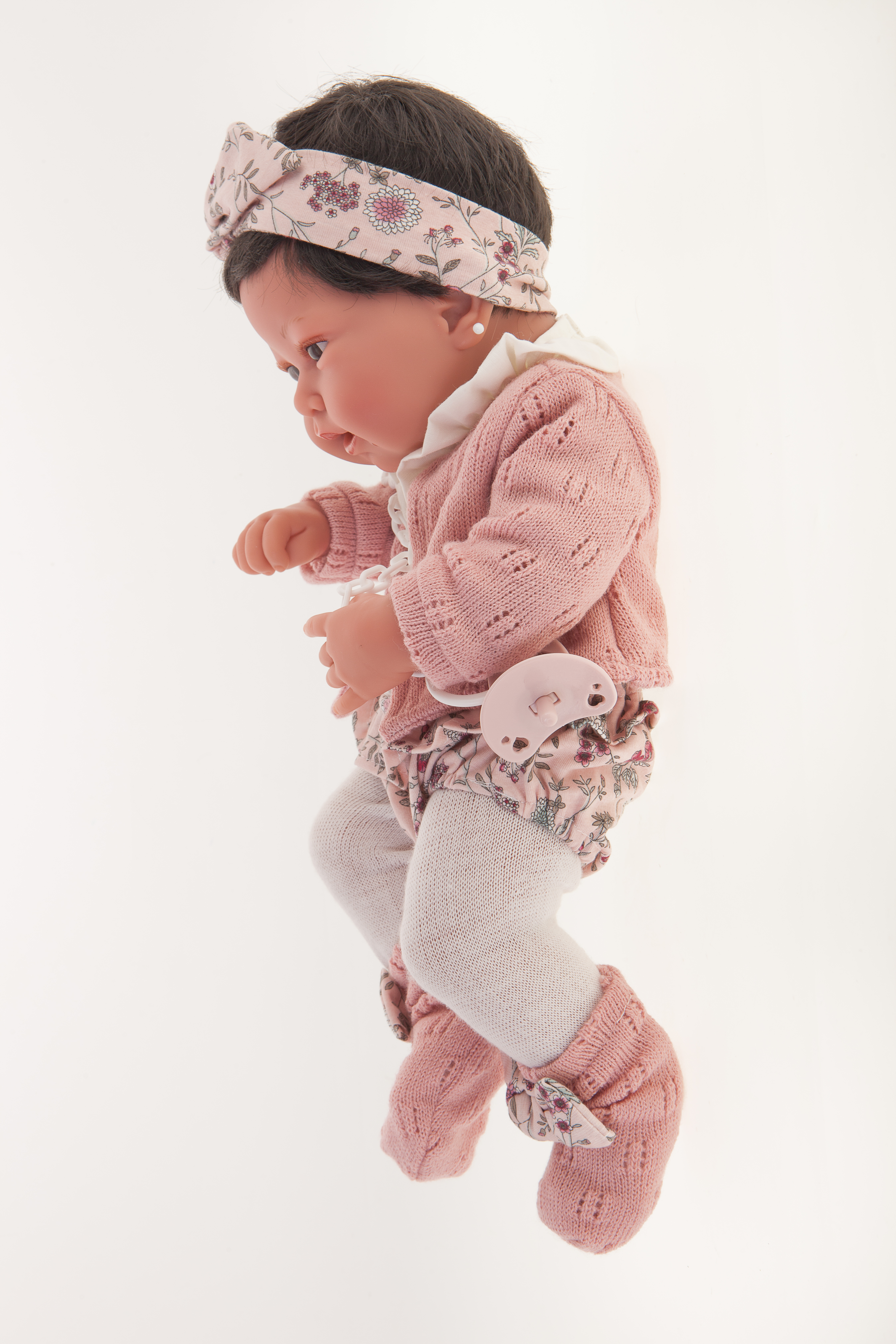 Antonio Juan Babypuppe Pipa, realistische Puppe mit dunklem Haar im rosa Strickoutfit, Seitenansicht mit Blumen-Stirnband