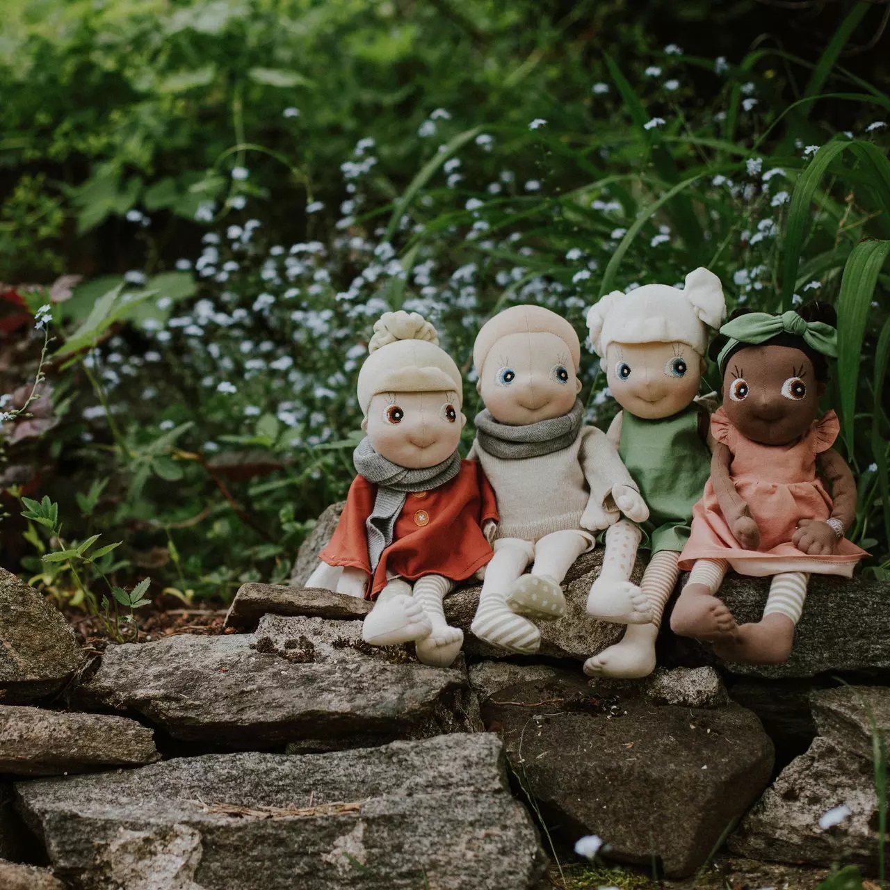 Four Rubens EcoBuds dolls in seasonal outfits sitting on a garden wall