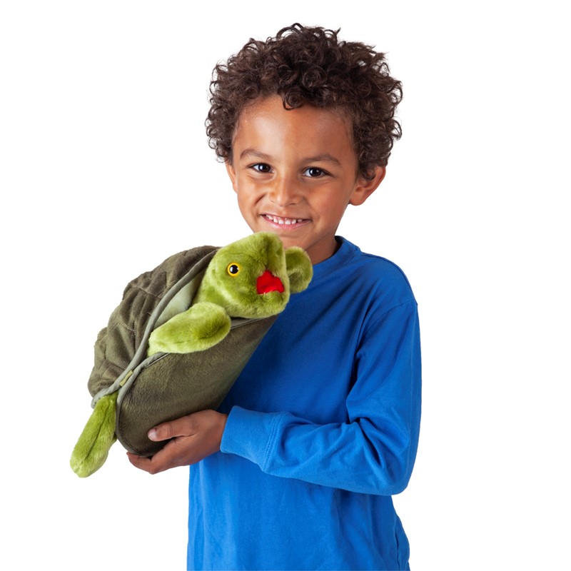 Junge im blauen Shirt hält die grüne Folkmanis Handpuppe große Schildkröte mit rotem Mund im Arm