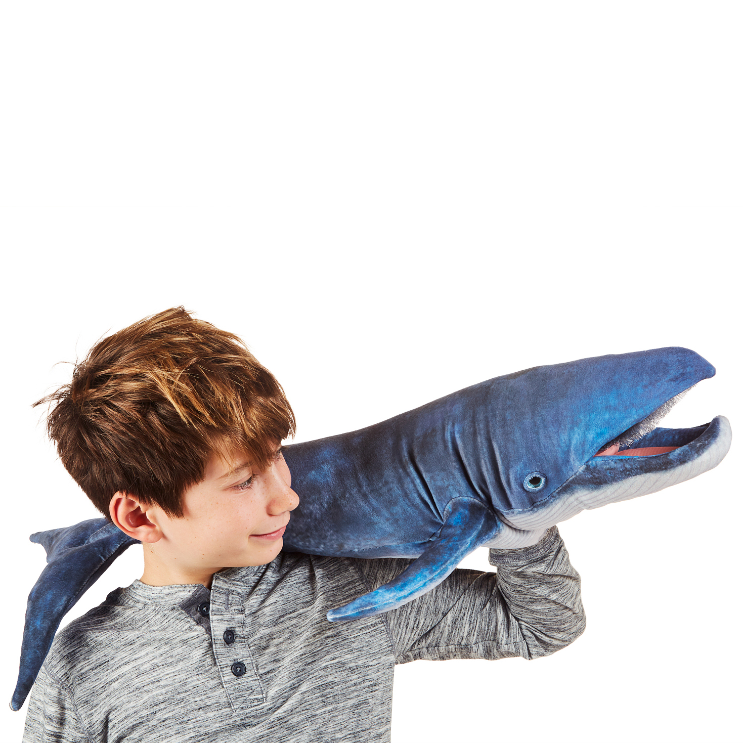 Boy operating the Folkmanis blue whale hand puppet with open mouth over his shoulder, detailed blue-grey plush surface