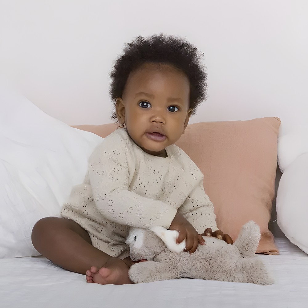 Cloud b Einschlafhilfe Dream Buddies Hund, Anwendungsfoto: Baby sitzt im Bett mit beigem Kuscheltier