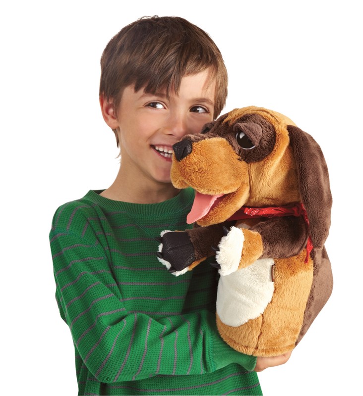 Lachender Junge hält Folkmanis Handpuppe Hund mit geöffnetem Maul, herausgestreckter Zunge und rotem Halsband in den Armen.