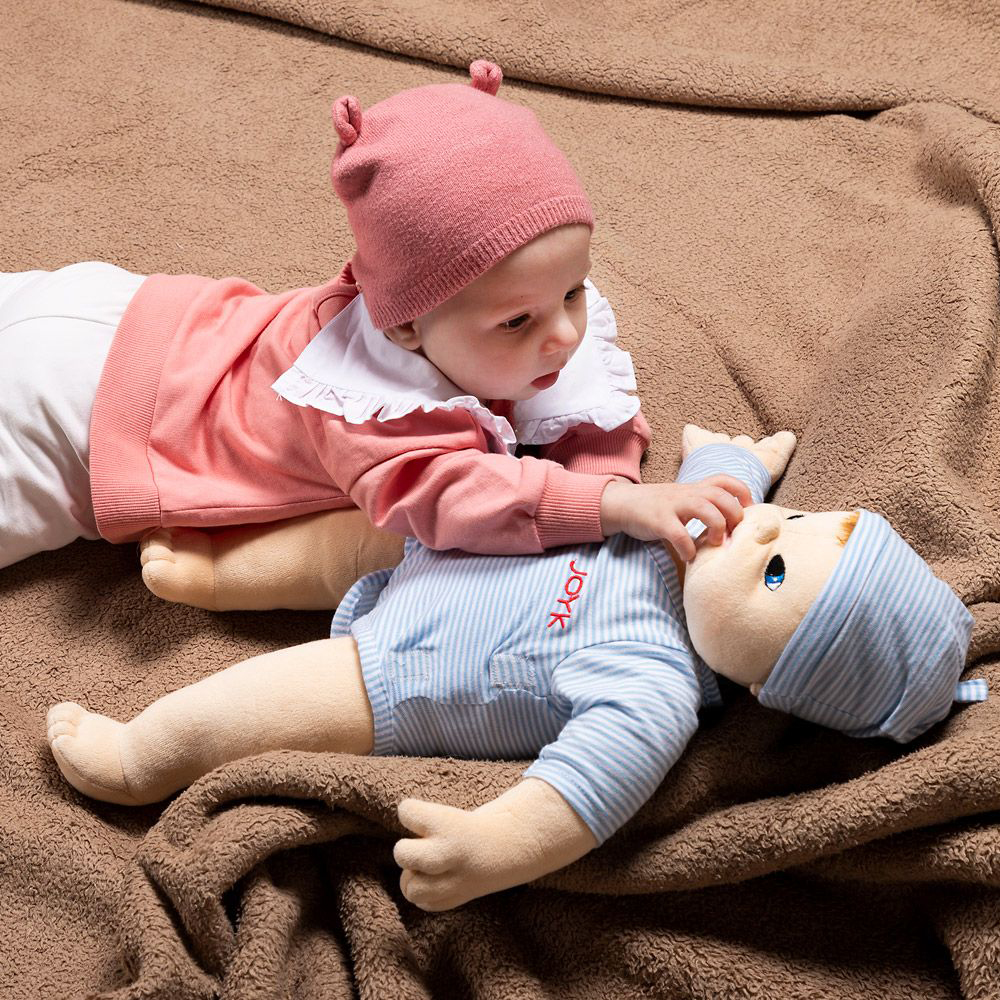 Baby betrachtet die gleich große Joyk Empathiepuppe Baby Elias auf einer Kuscheldecke