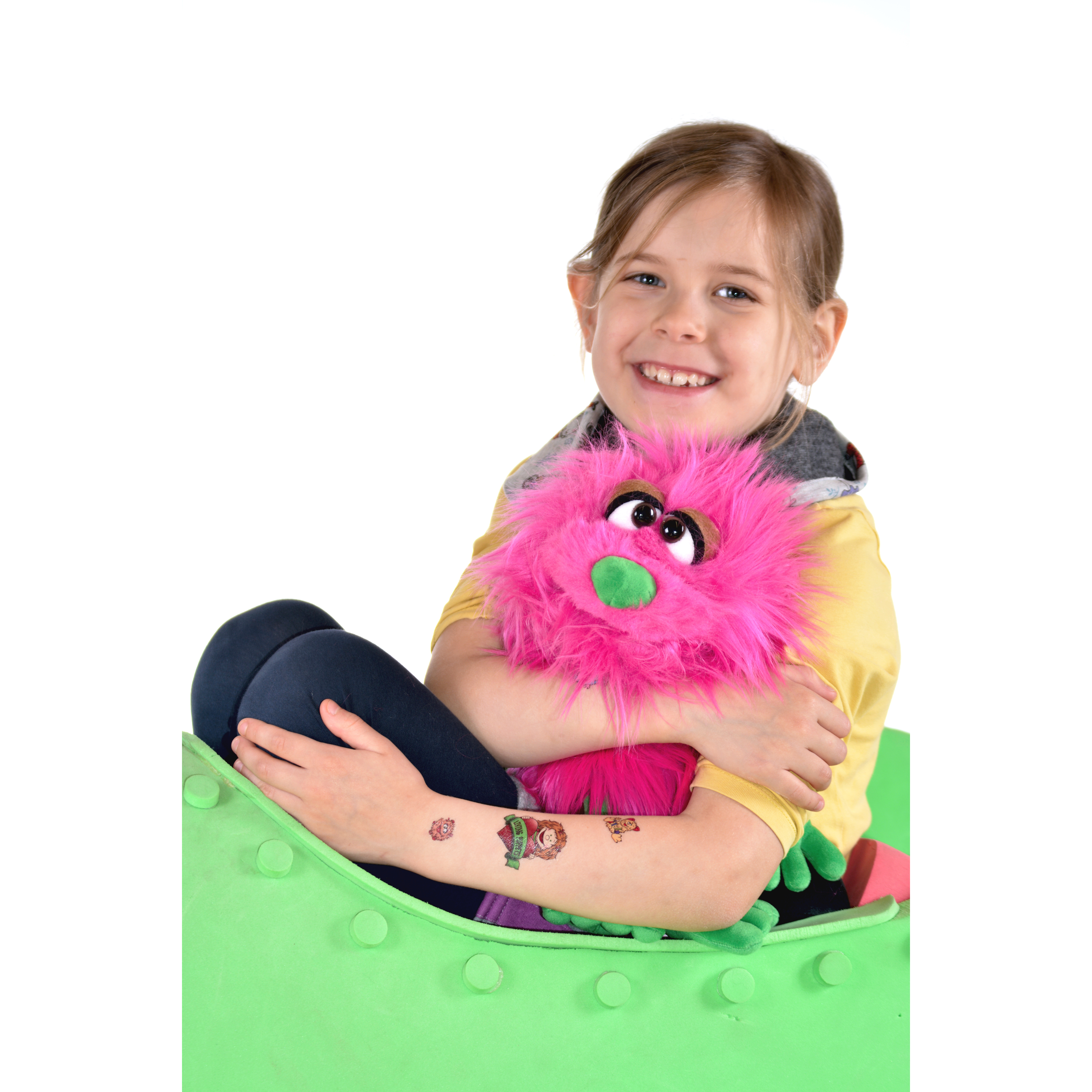 Child with a Living Puppets tattoo on their arm hugging a pink shaggy monster hand puppet, usage example