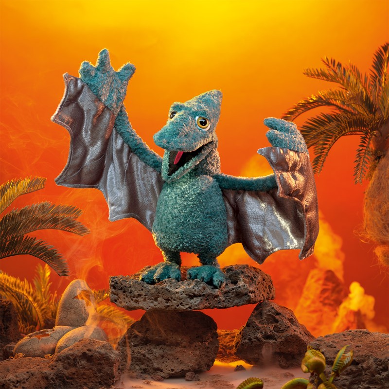 Folkmanis Handpuppe Flugsaurier in Blaugrün mit ausgebreiteten Flügeln auf Lavagestein vor orangerotem Vulkanhintergrund