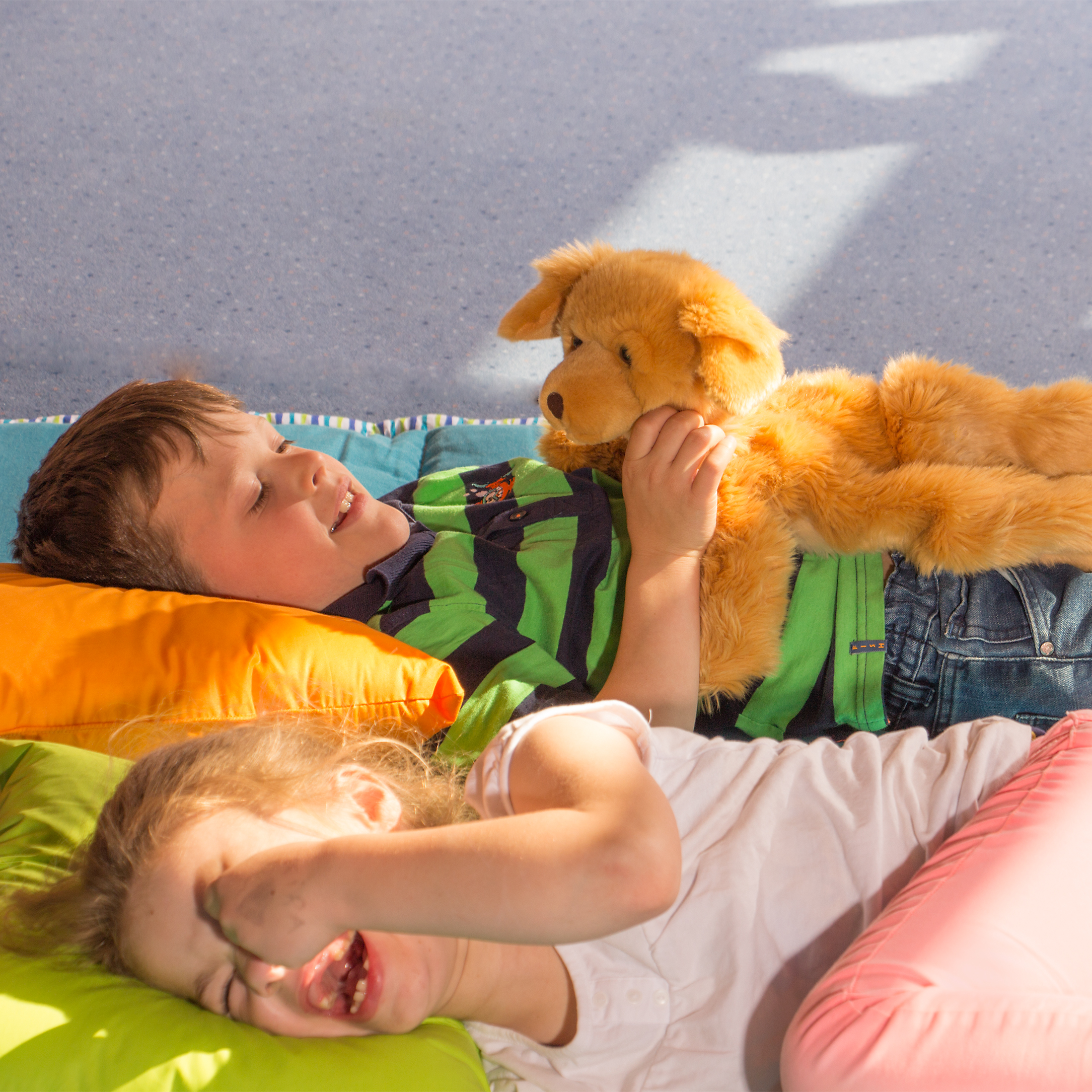 Children playing with the Joyk empathy doll Brando, a golden-brown dog, lying down