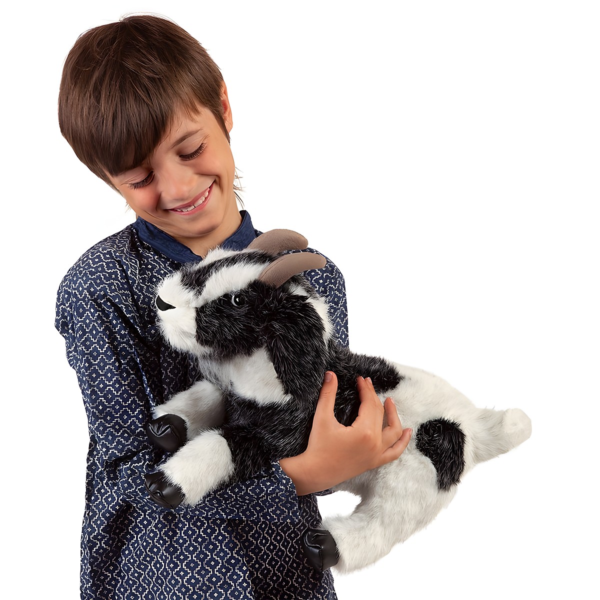 Junge hält Folkmanis Handpuppe Ziege mit schwarz-weißem Fell und braunen Hörnern lächelnd in den Armen