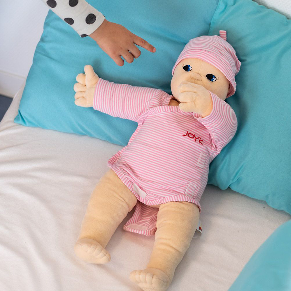 Joyk Empathiepuppe Baby Lilly liegt auf einem Bett mit türkisfarbenen Kissen