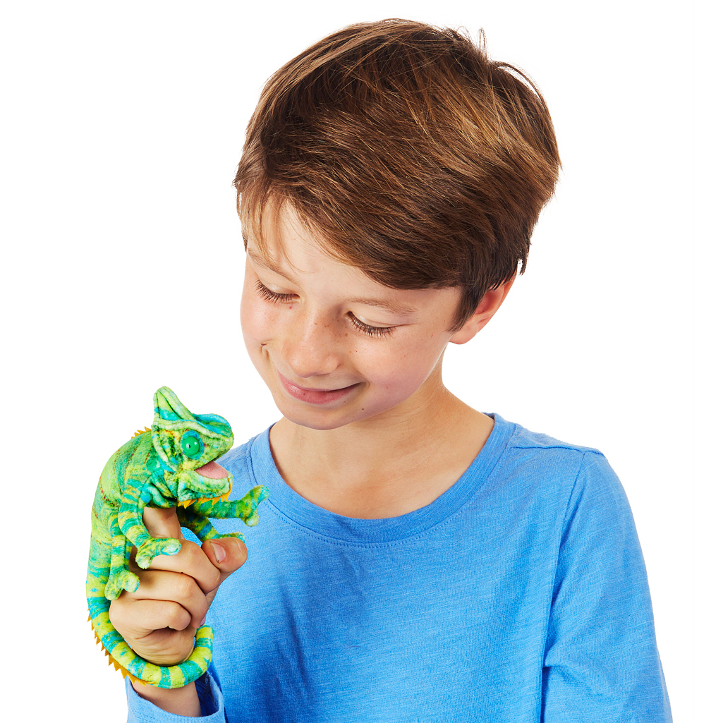 Boy holding a Folkmanis mini chameleon finger puppet in green and blue on his index finger, smiling down at it