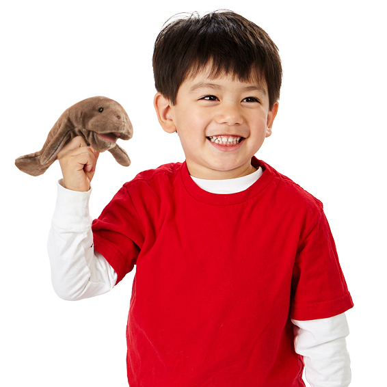 Smiling boy holding a Folkmanis mini manatee finger puppet in brown on his raised index finger