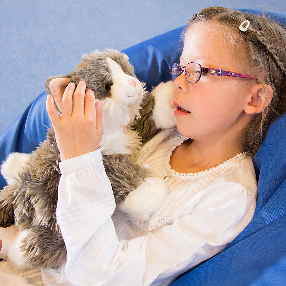 Kind hält die Joyk Empathiepuppe Billy, eine grau-weiße Plüschkatze, im Arm