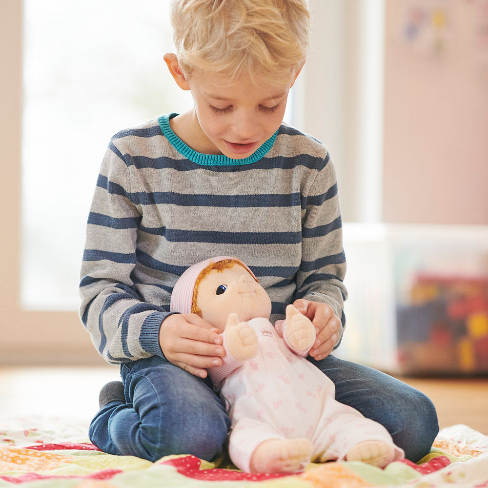 Kind hält die Joyk Empathiepuppe Baby Emma behutsam auf dem Schoß