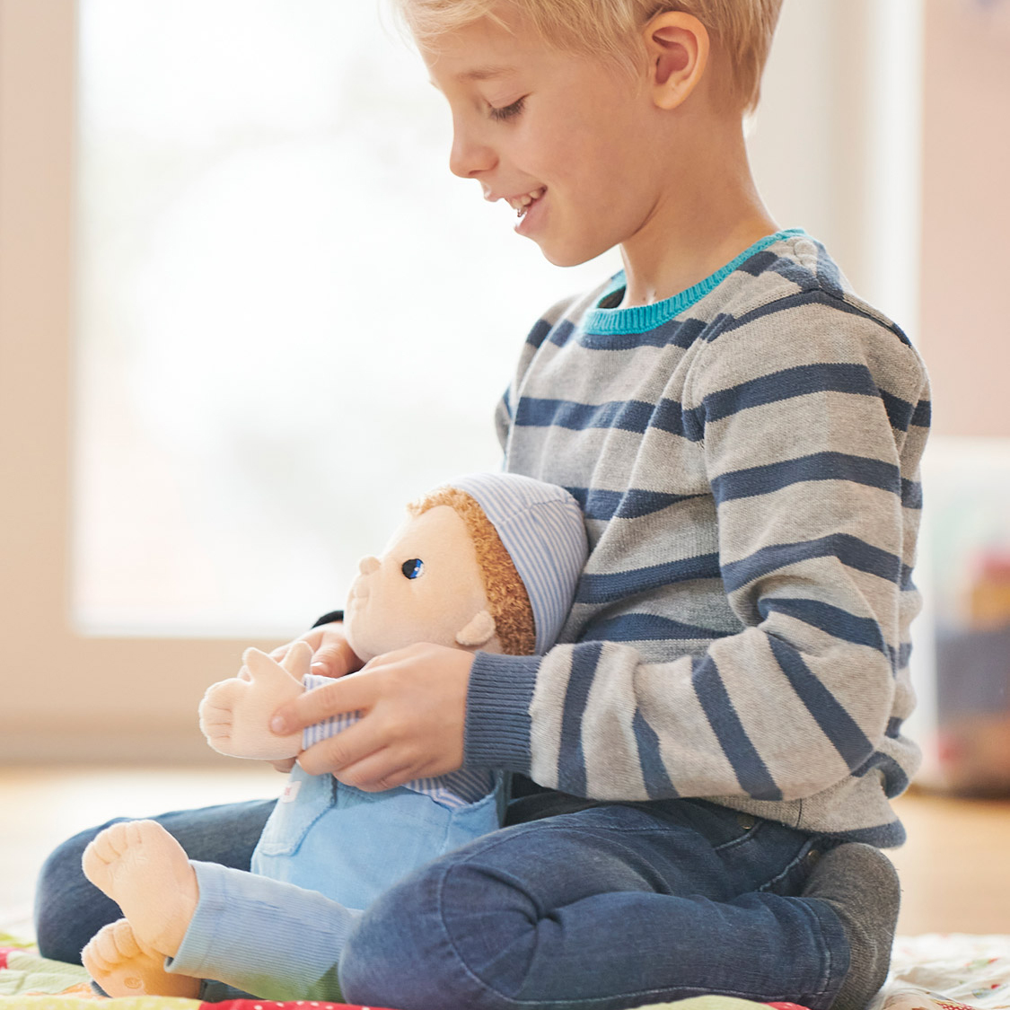 Kind spielt mit der Joyk Empathiepuppe Baby Jack auf einer Spieldecke