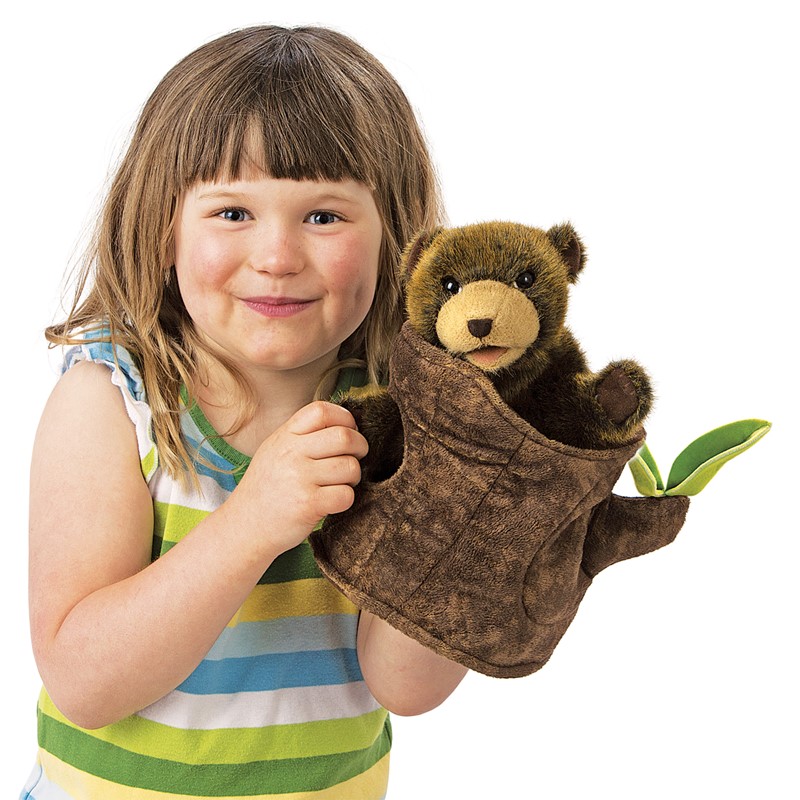 Folkmanis Handpuppe Bär im Baumstumpf: Kind hält braune Plüsch-Bärenfigur, die aus einem Baumstumpf-Handpuppenüberzug mit grünen Blättern lugt.