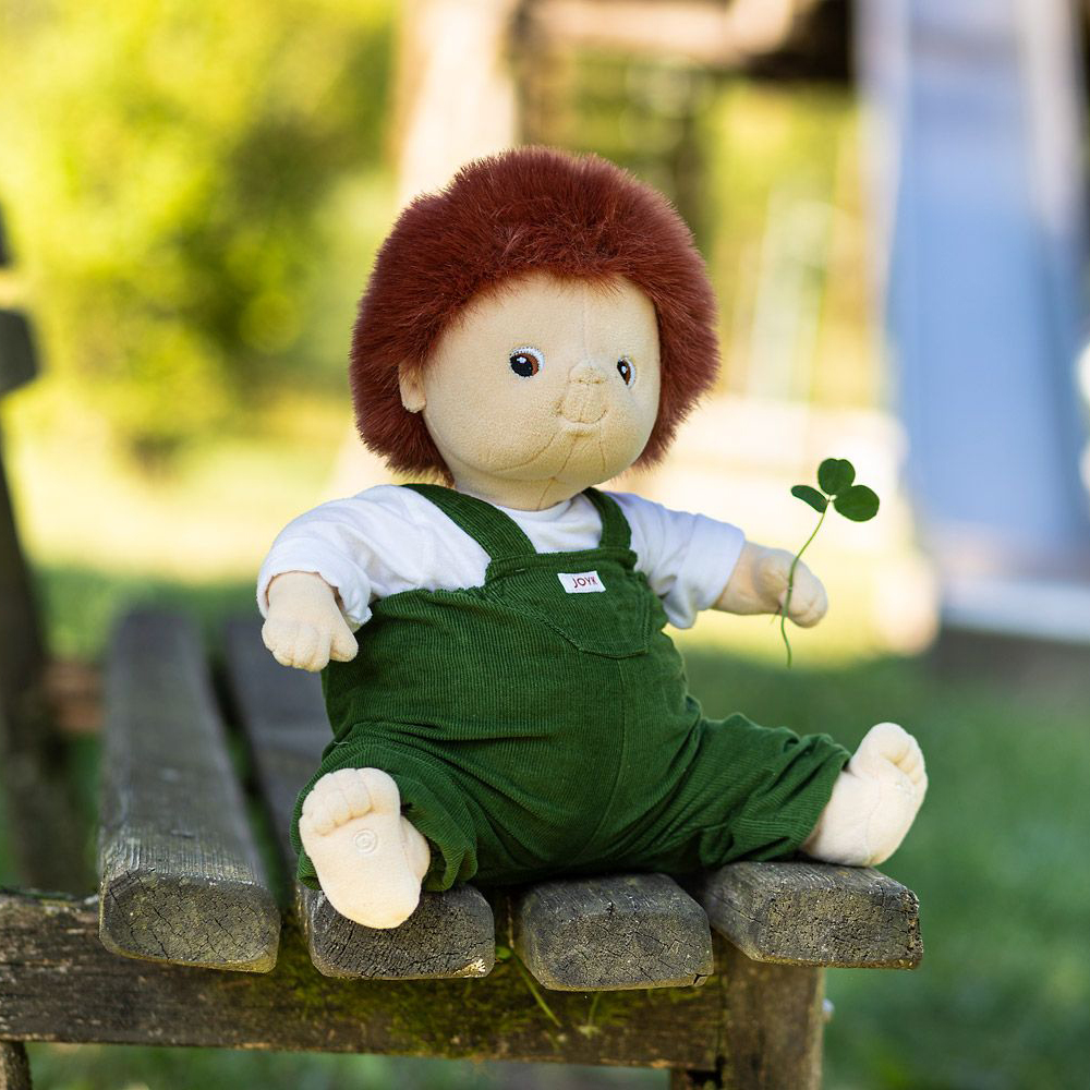 The Joyk empathy doll Sam sitting with a cloverleaf on a garden bench