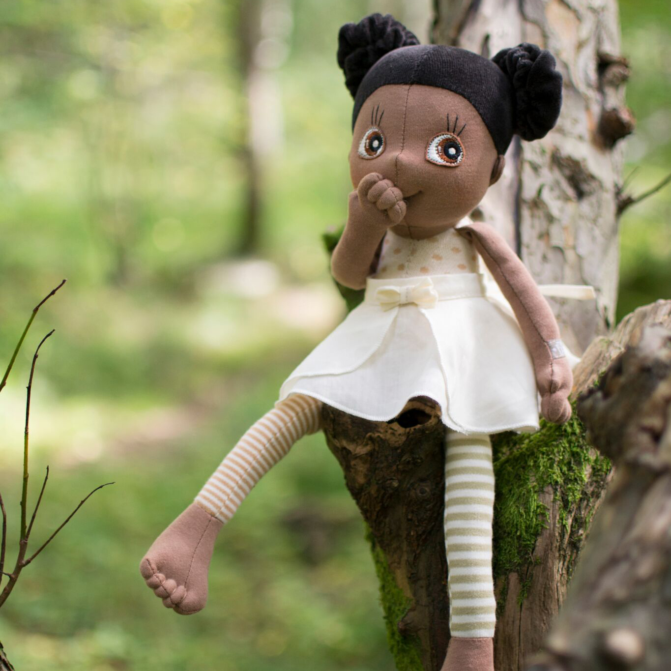 The Rubens EcoBuds doll Poppy sitting at a tree stump in the forest