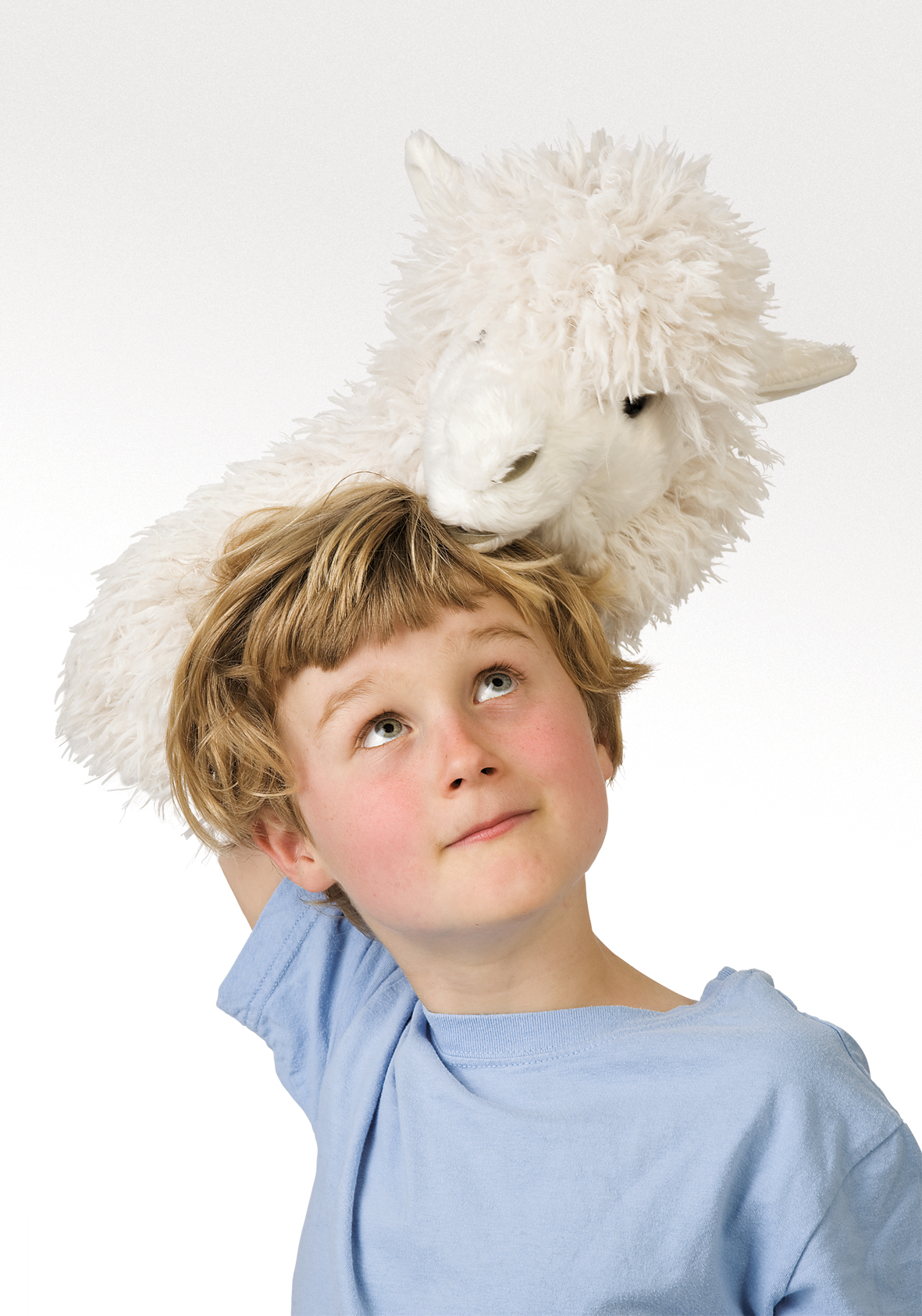Child balancing a white Folkmanis alpaca hand puppet with shaggy fur on their head, looking up with a smile