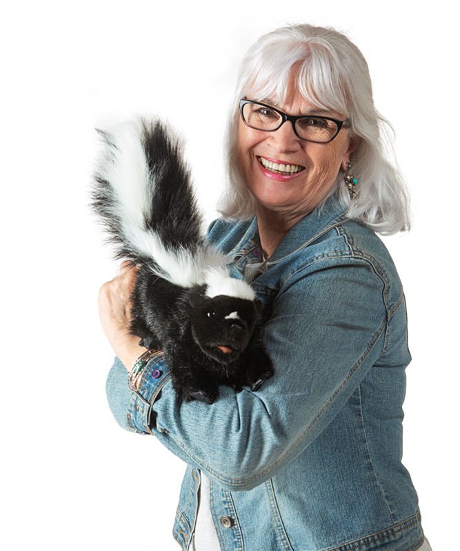 Lächelnde Frau hält die Folkmanis Handpuppe Stinktier mit schwarz-weißem Fell und buschigem Schwanz im Arm.