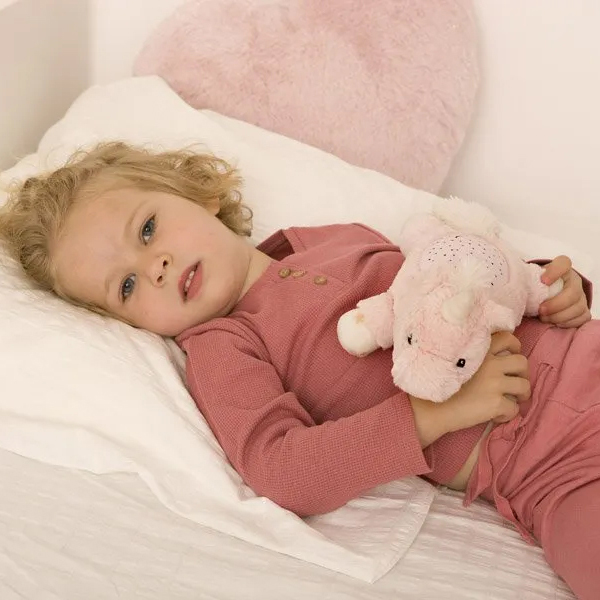 Cloud b Einschlafhilfe Dream Buddies Einhorn, Anwendungsfoto: Kleinkind liegt im Bett und umarmt rosa Kuscheltier