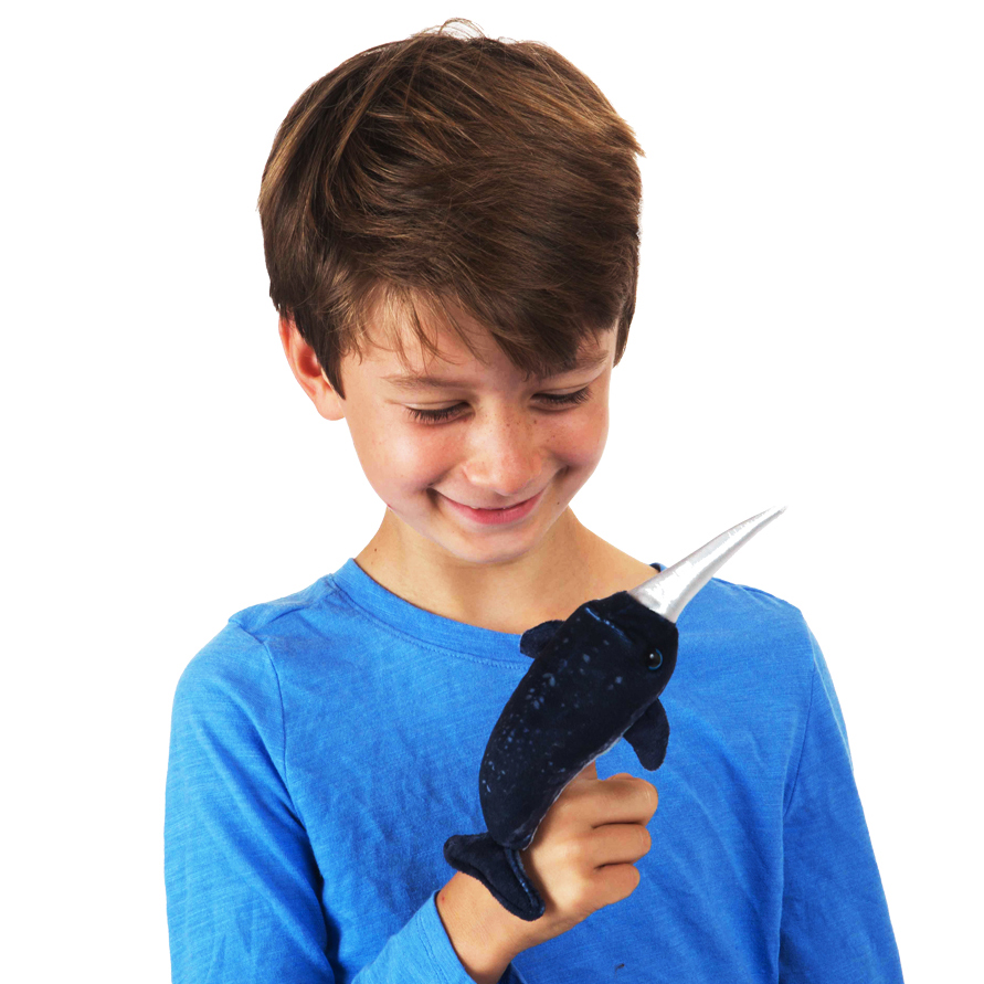 Junge mit blauem Pullover hält lächelnd die Folkmanis Fingerpuppe mini Narwal in Dunkelblau mit silbernem Horn am Finger.