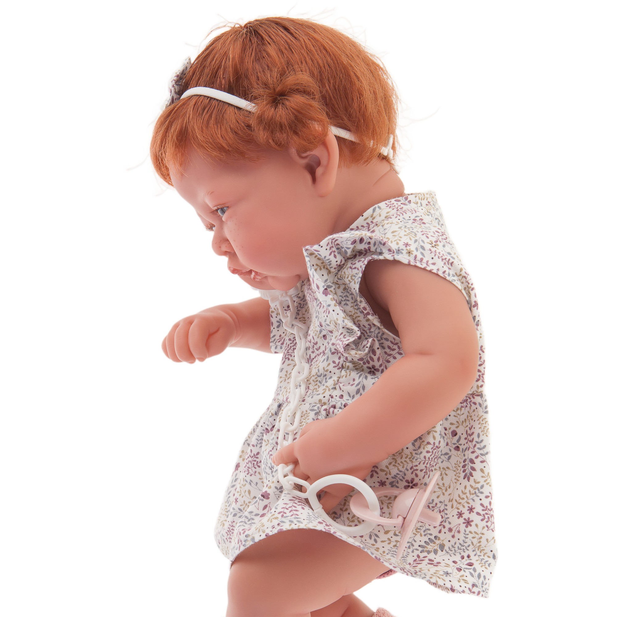 Antonio Juan baby doll New Born, realistic doll with red hair in a floral dress, side view with pink knit socks