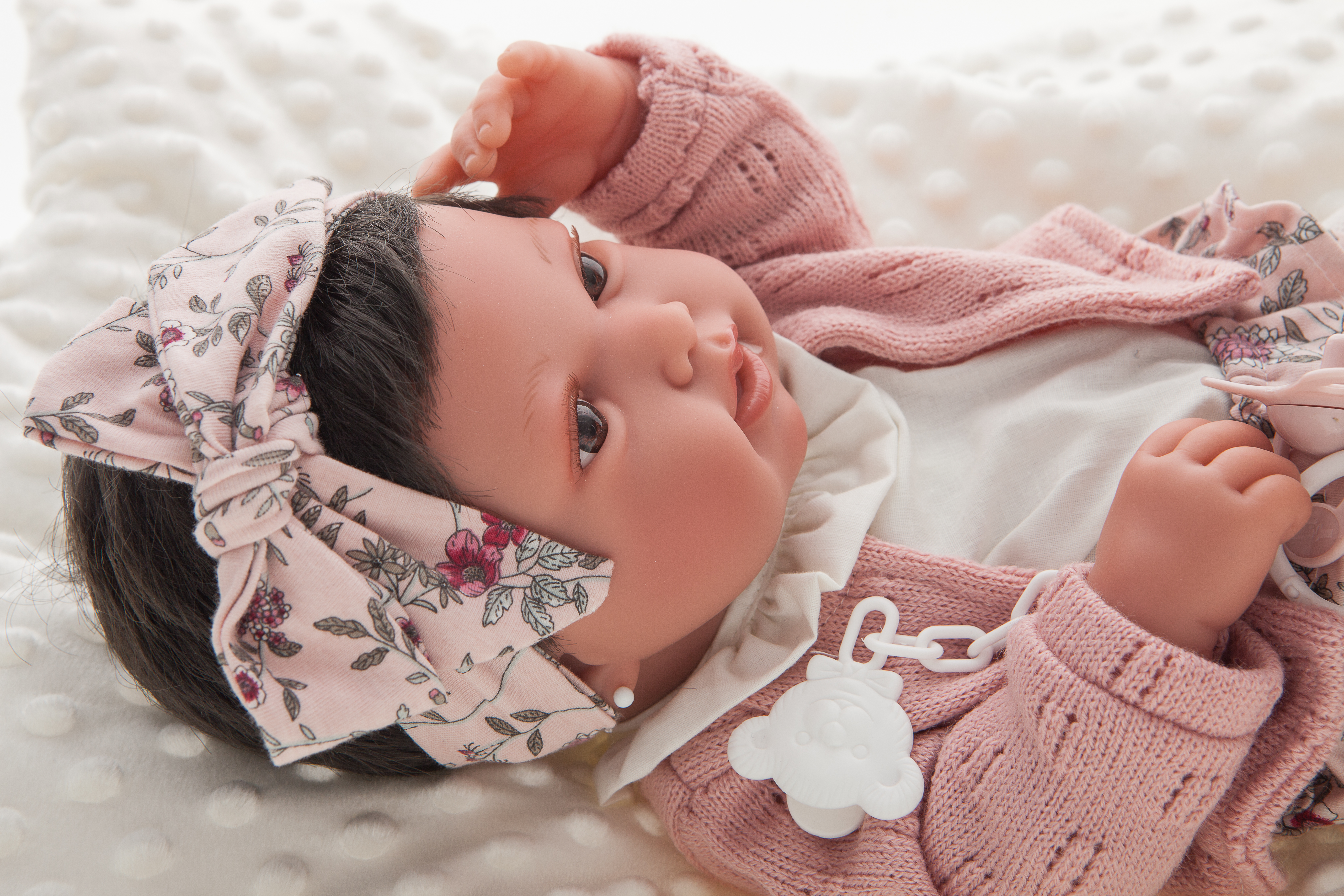 Antonio Juan Babypuppe Pipa, Gesichts-Nahaufnahme mit dunklem Haar, Blumen-Schleife und rosa Strickjacke