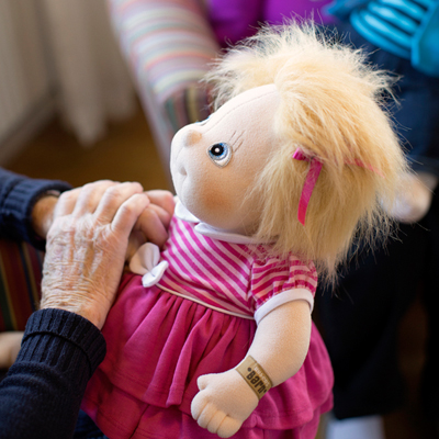 Senior lady touching the Rubens Barn Original doll Ida in a pink dress
