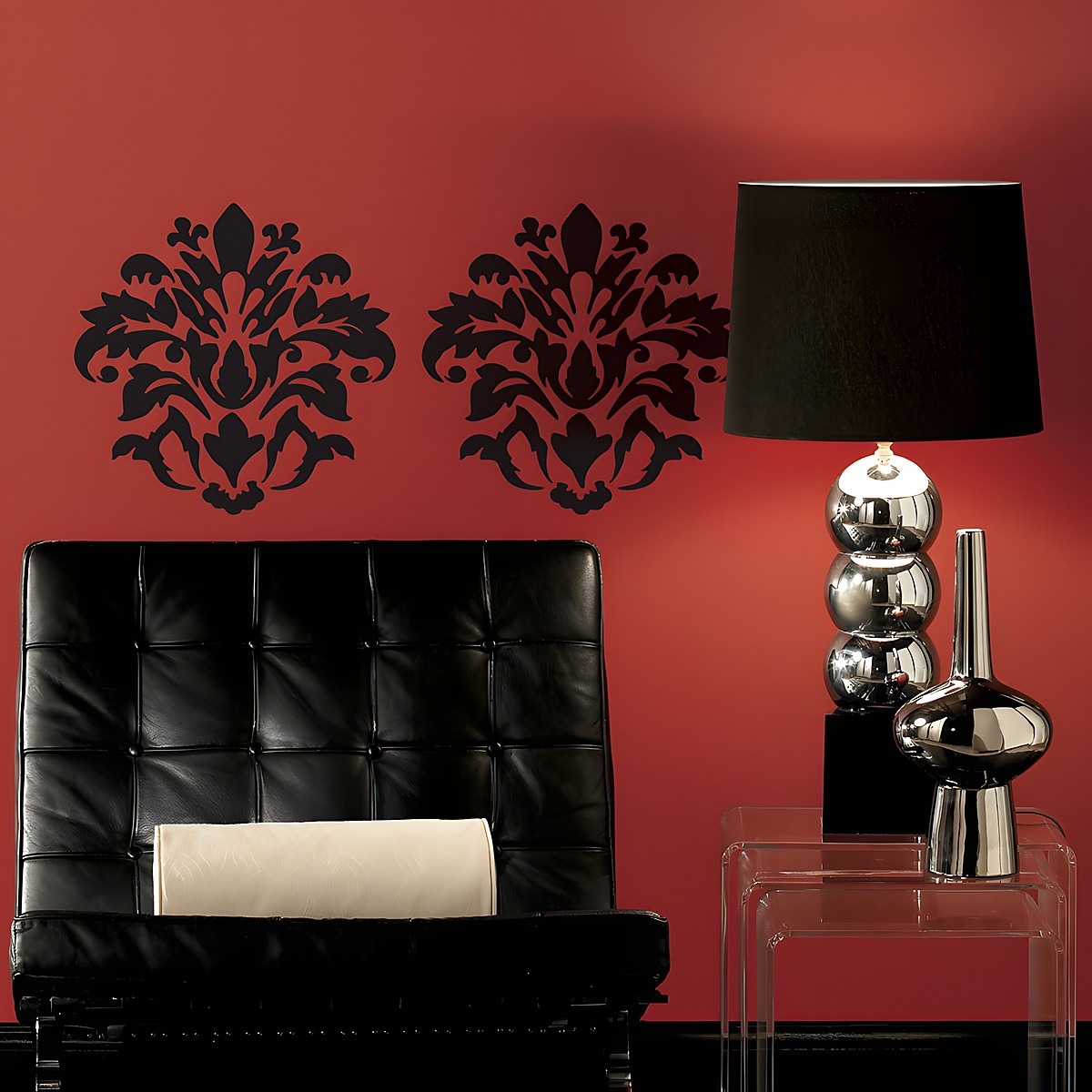 RoomMates wall decal Damask Peel & Stick, two black damask ornaments on a red wall behind a black leather armchair
