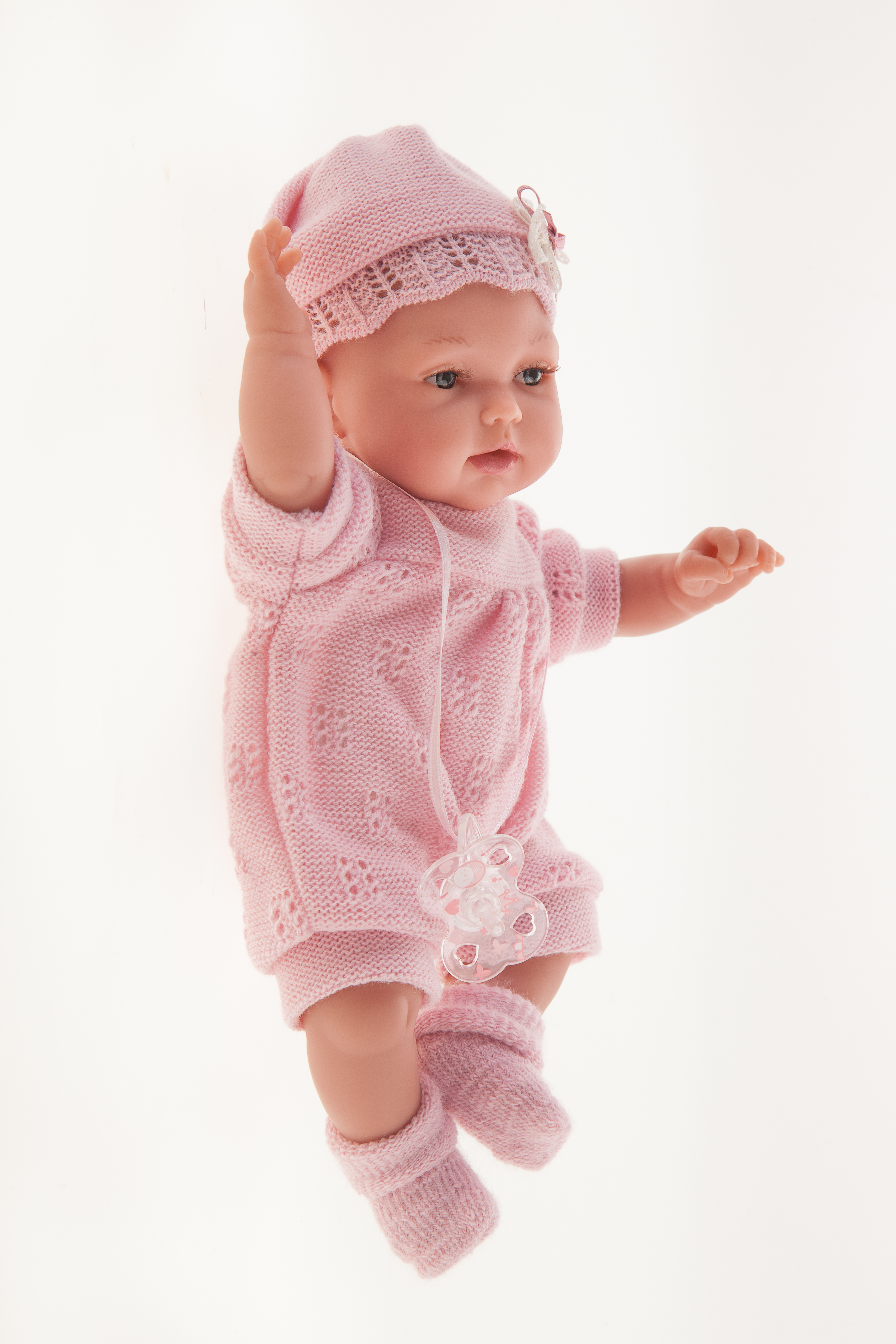 Antonio Juan Babypuppe Peke, realistische Puppe im rosa Strickset, Seitenansicht mit erhobenem Arm über dem Kopf vor weißem Hintergrund
