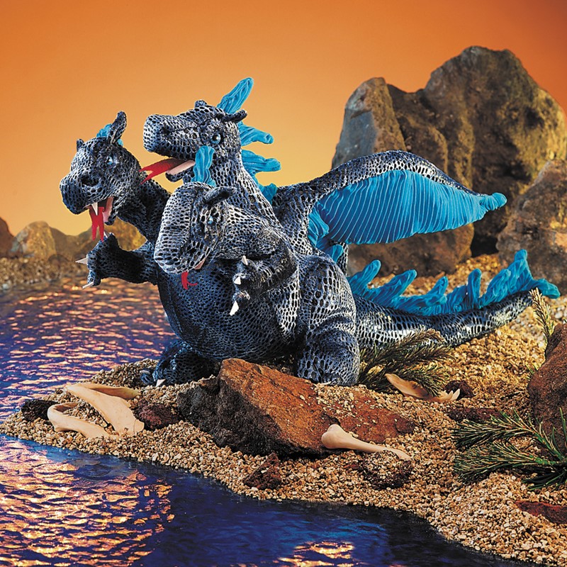 Folkmanis hand puppet three-headed dragon in dark blue with blue wings and spines, lying in front of a rocky backdrop